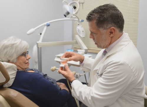Dentist showing a dental model to a woman seated in a dental chair