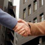 Two people in coats shaking hands outdoors