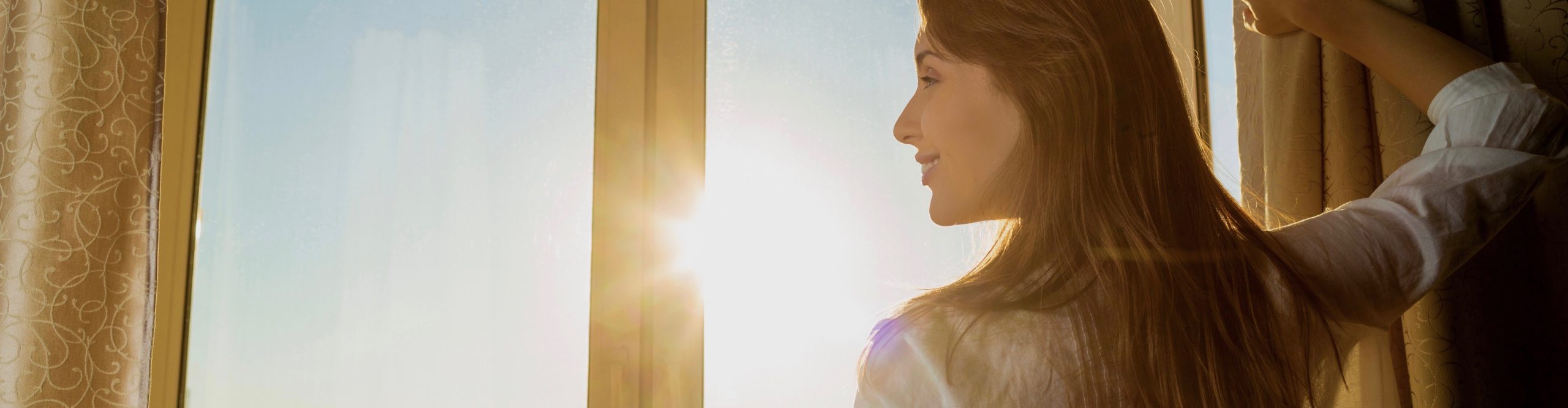 Woman opening curtains beside a sunlit window