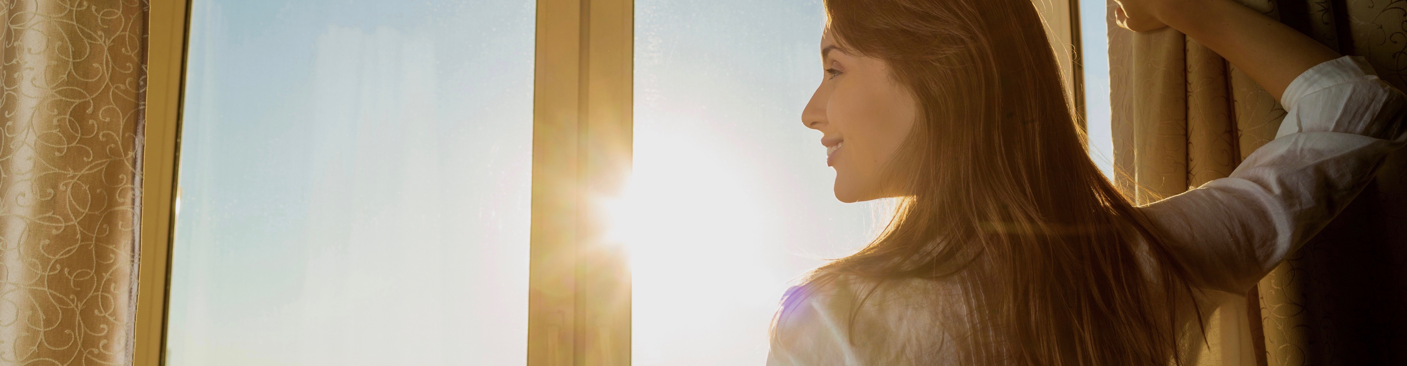 Woman opening curtains beside a sunlit window